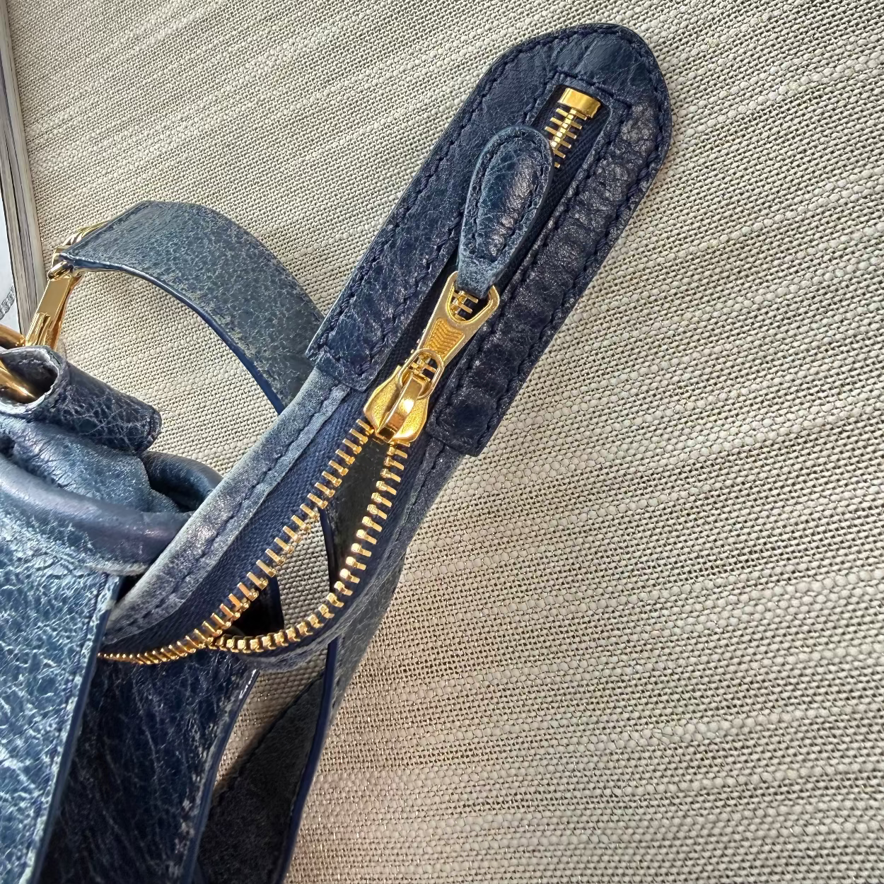Close-up of a blue handbag with gold zipper on a beige textured surface