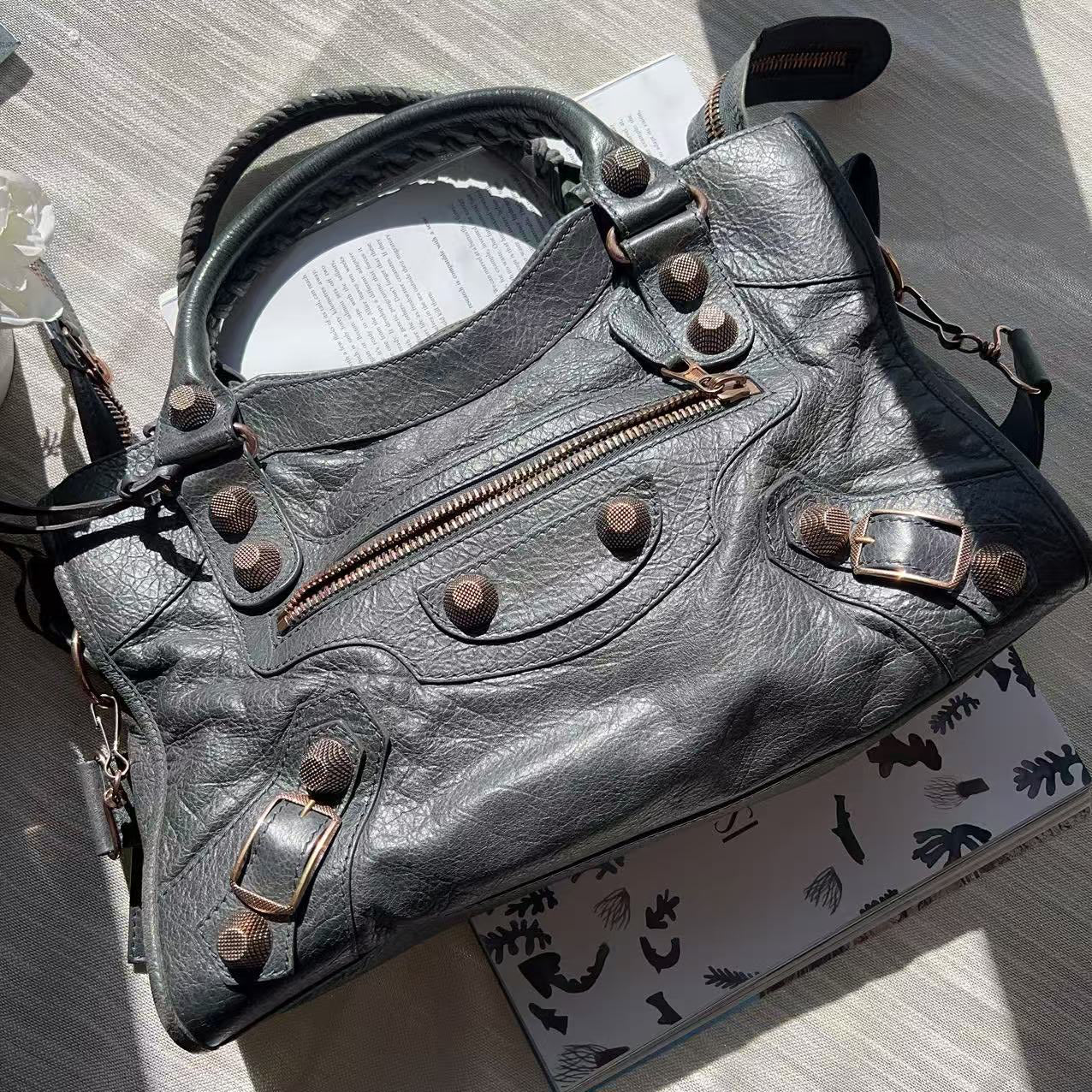 Gray leather handbag with brass fixtures on a patterned surface