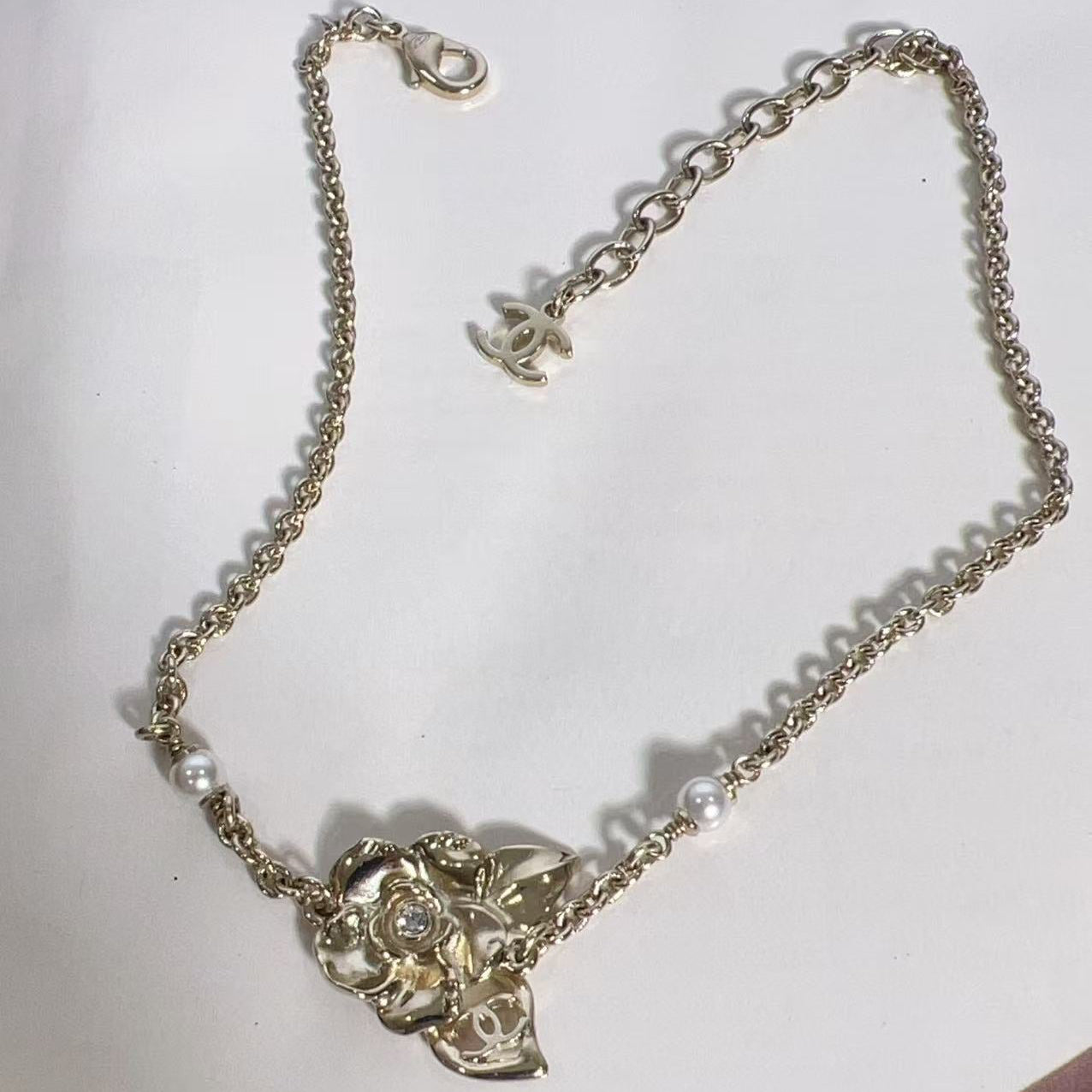 Gold necklace with floral design and pearl-like beads on a white background