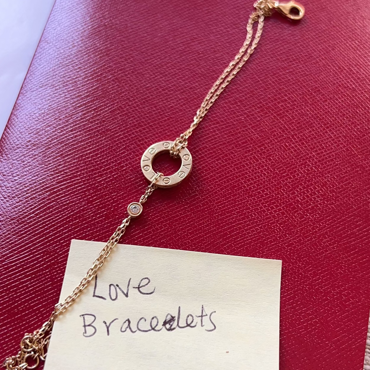 Gold bracelet on a piece of paper labeled 'Love Bracelets' against a red background with 'Cartier' branding.