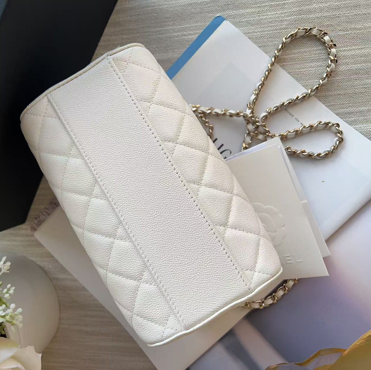 White quilted handbag with a gold chain on a textured surface