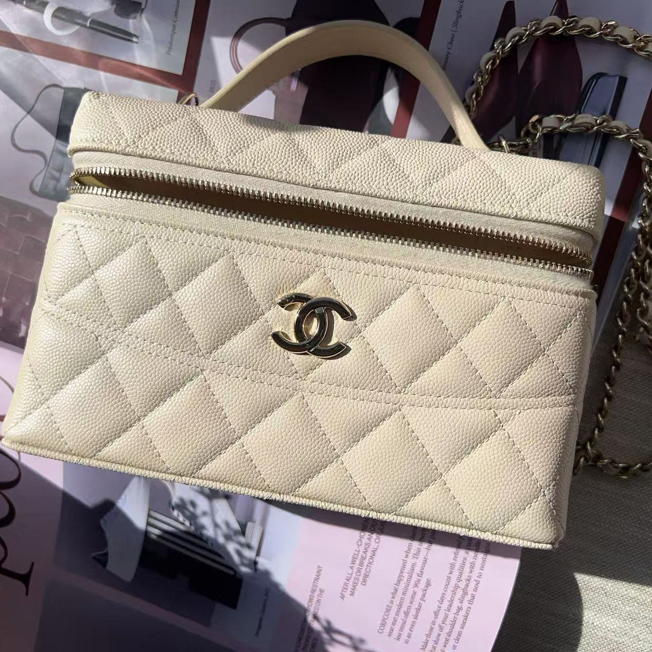 Beige quilted handbag with gold chain on a magazine
