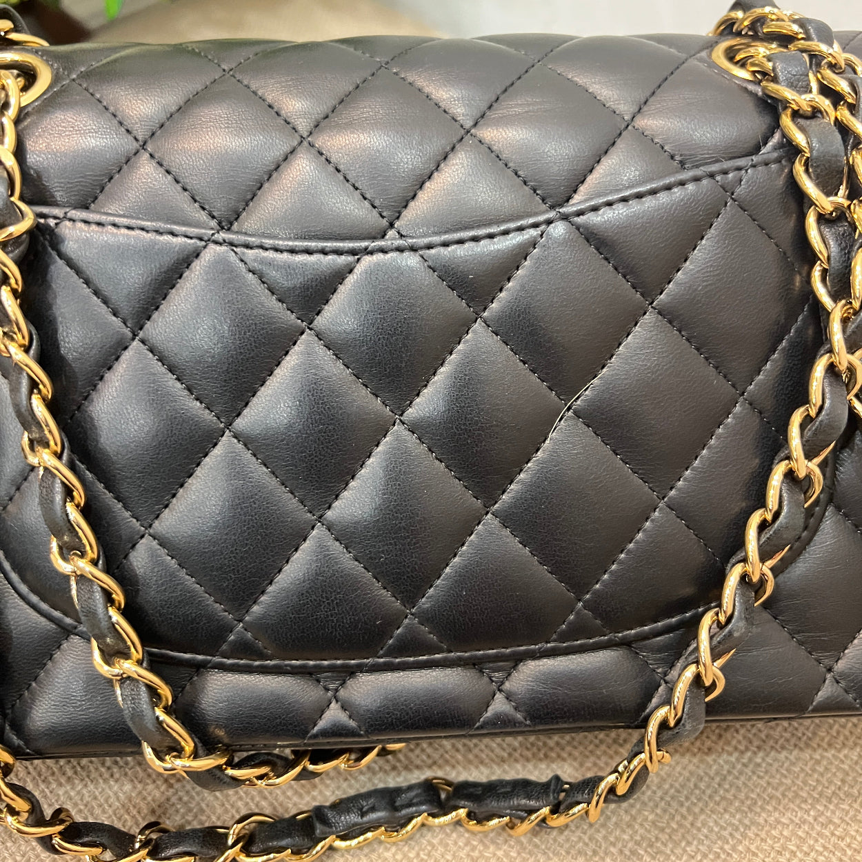 Black quilted handbag with gold chain strap on a neutral background