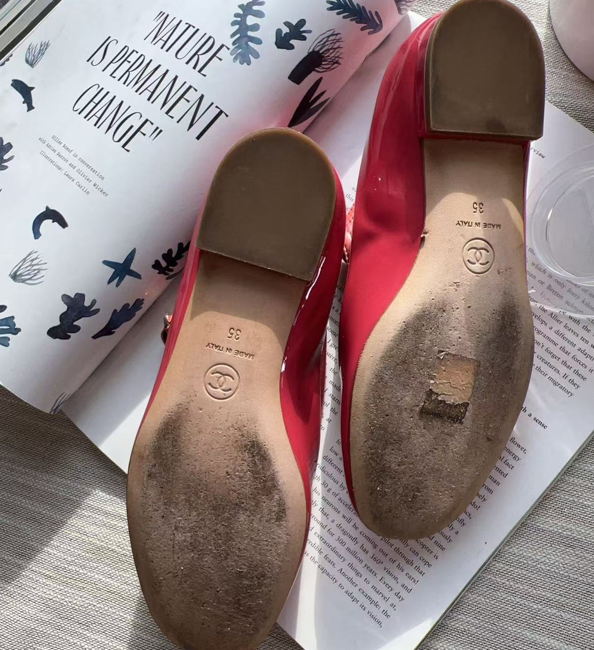 A pair of red Mary Jane flats shown from the bottom, resting on open books. The soles show a visible logo stamp and a noticeable scuff on the sole of the right shoe.