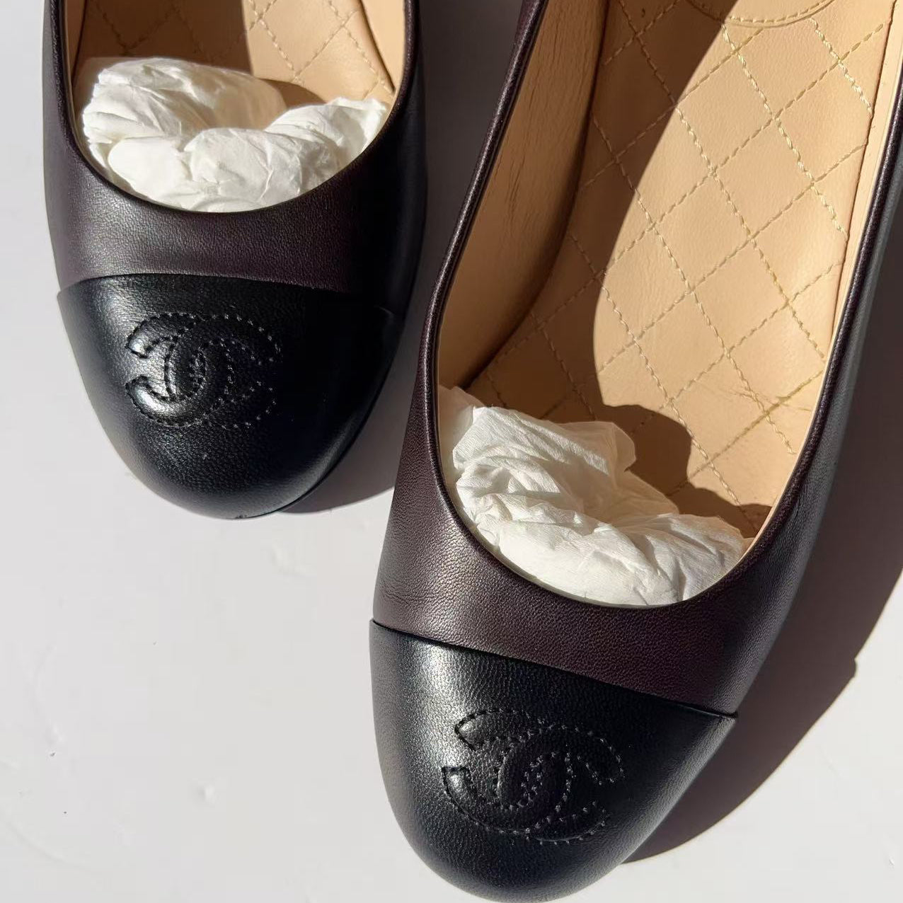 Pair of black Chanel shoes with quilted interior on a light gray background