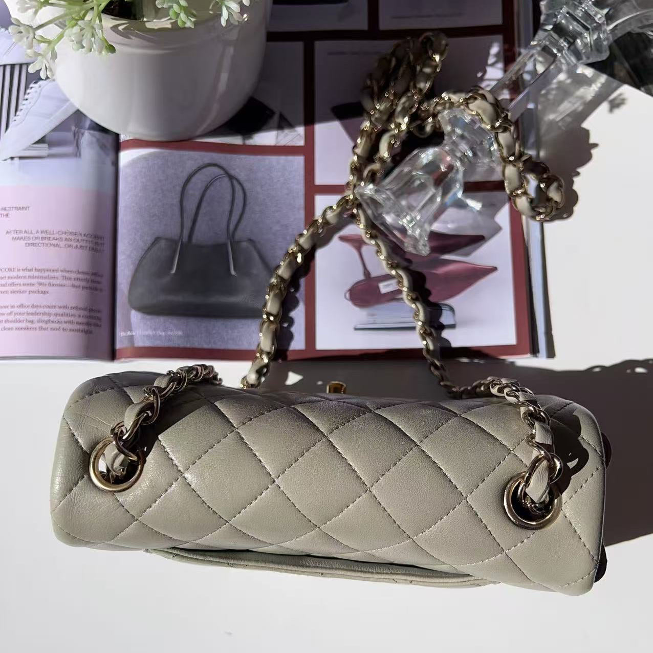 Light gray quilted handbag with gold chain strap on a white surface.