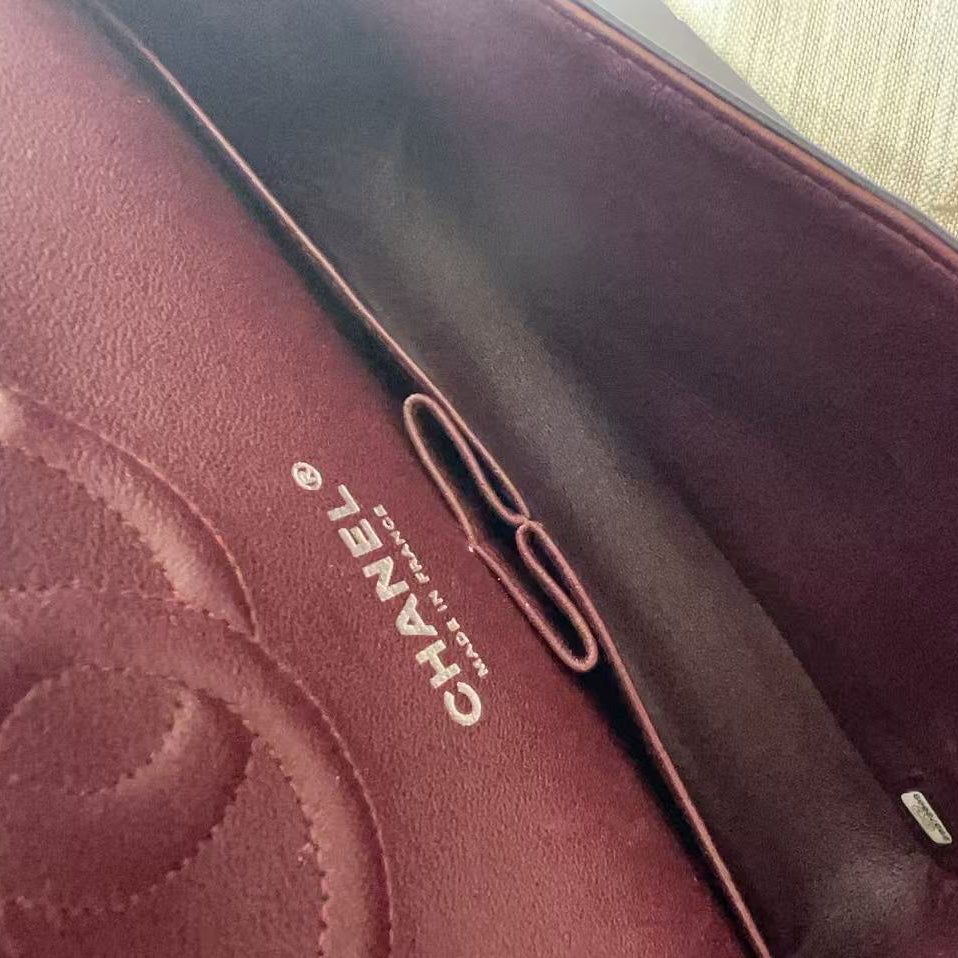 Close-up of a burgundy leather Chanel bag interior showing the CHANEL logo, a dark brown leather divider, and a small silver metal accent.