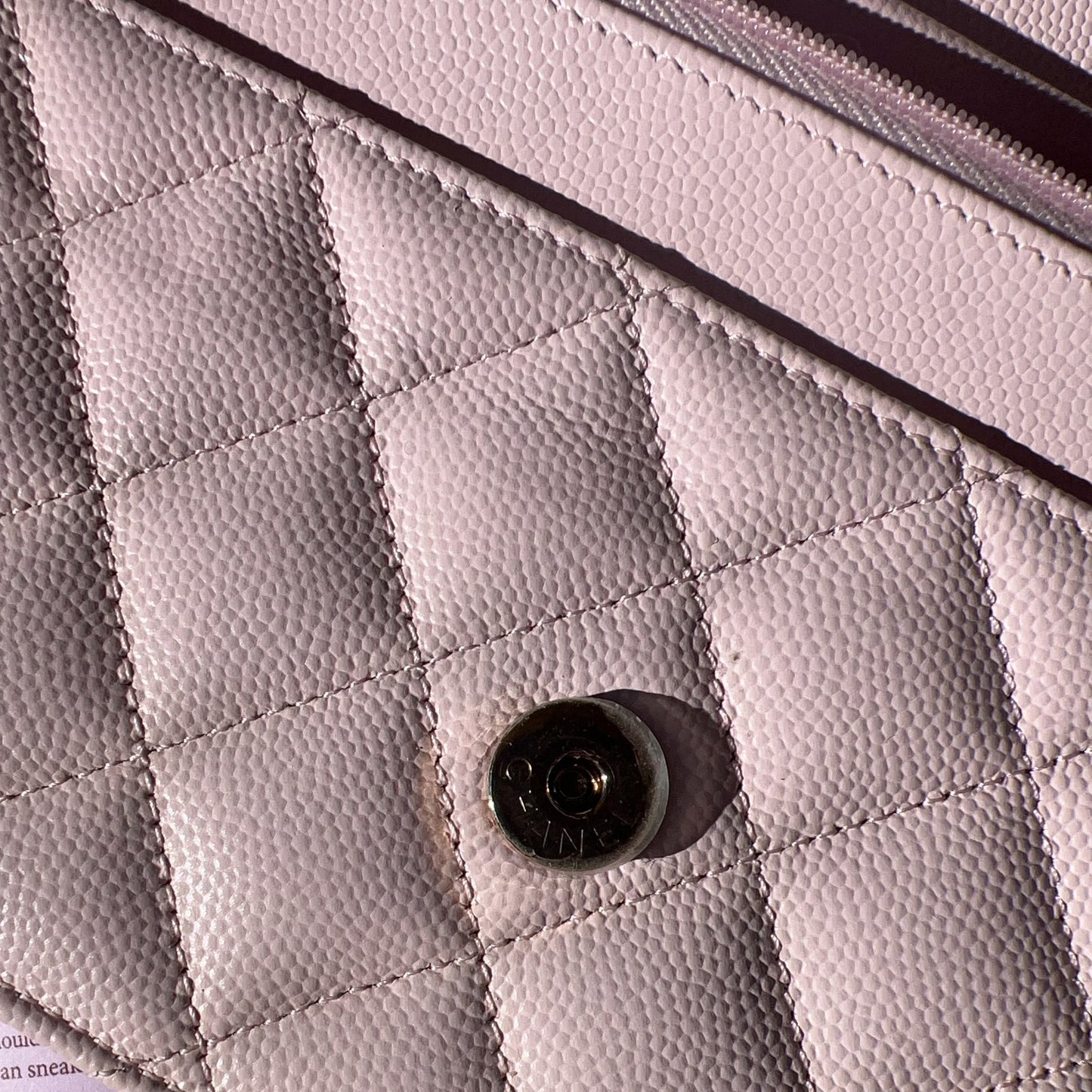 Close-up of a quilted pink handbag with a button on a light purple background