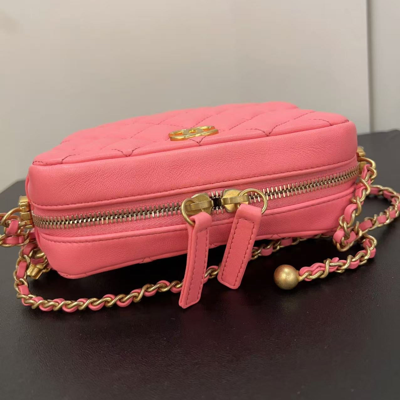 Pink handbag with gold chain strap on a dark surface