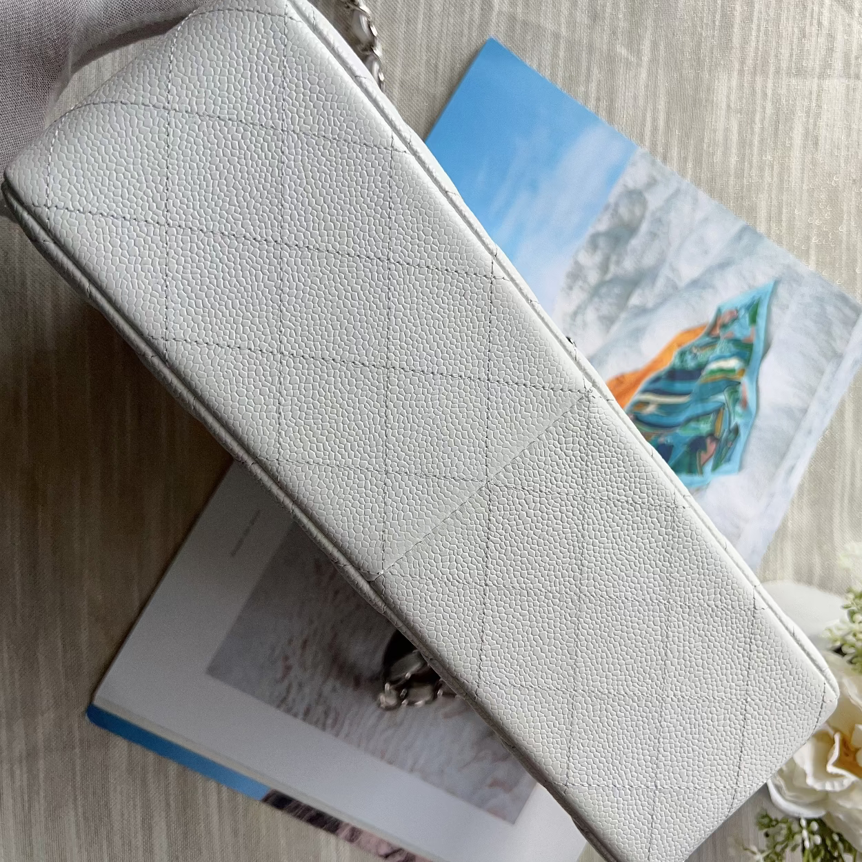 White wallet on a surface with a magazine and flowers