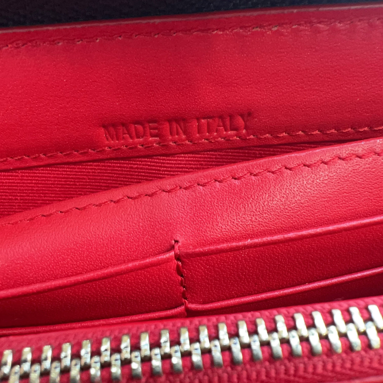 Close-up of a red leather wallet with 'MADE IN ITALY' text and zipper details.
