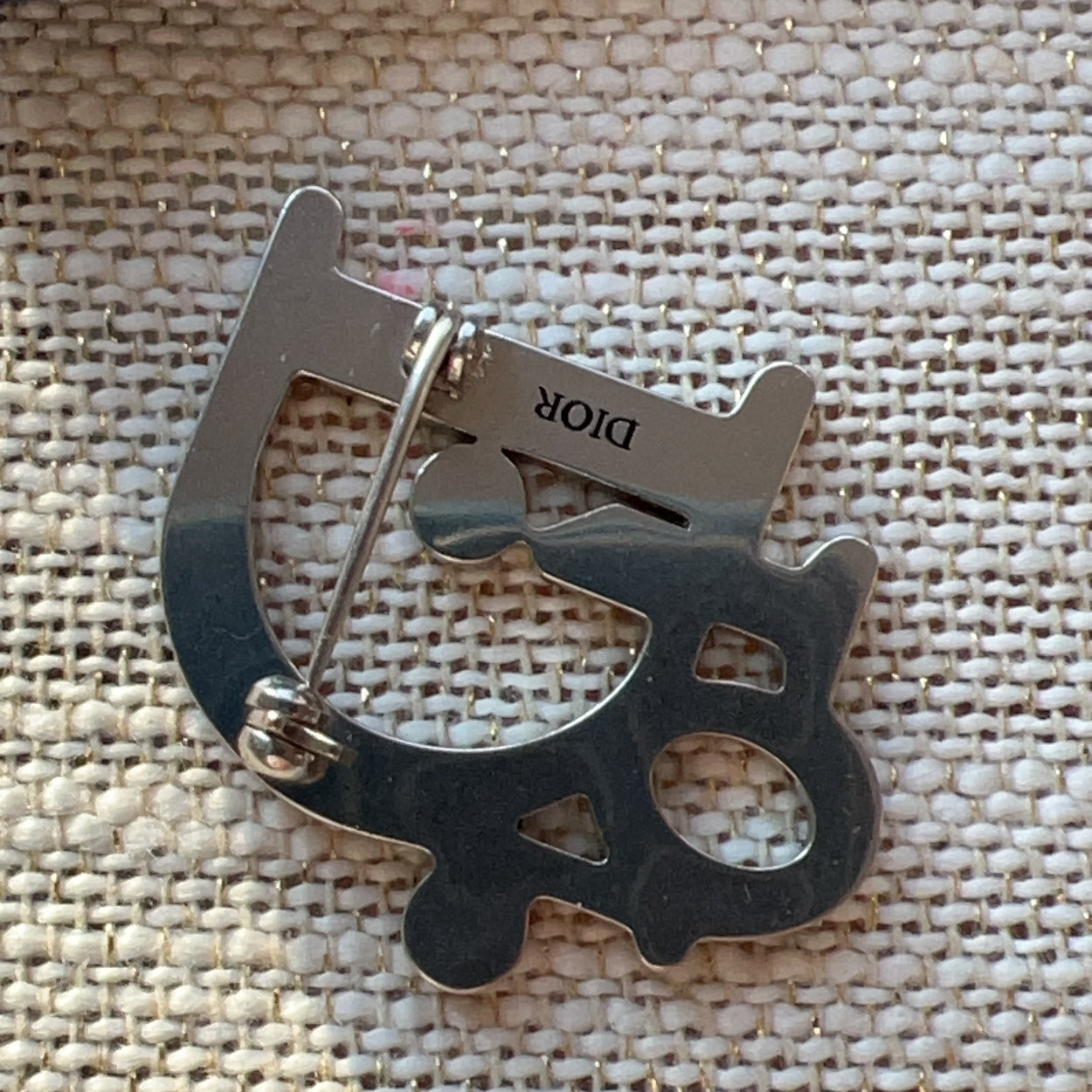Metallic keychain with 'DIOR' branding on a textured fabric background