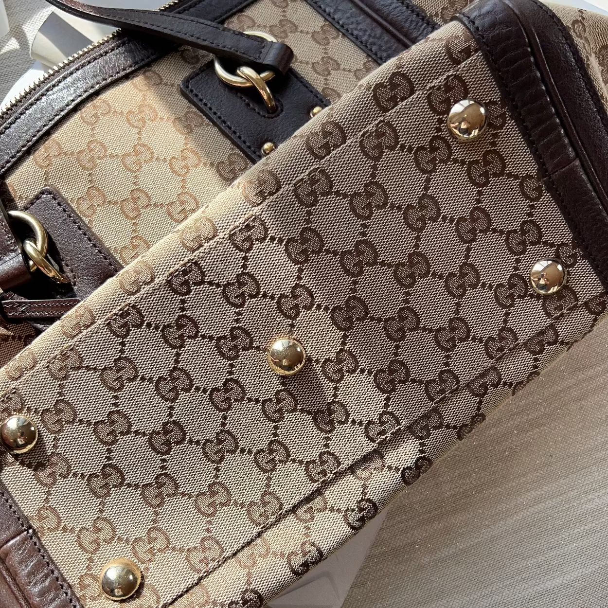Close-up of a patterned handbag with gold accents on a light wooden surface.