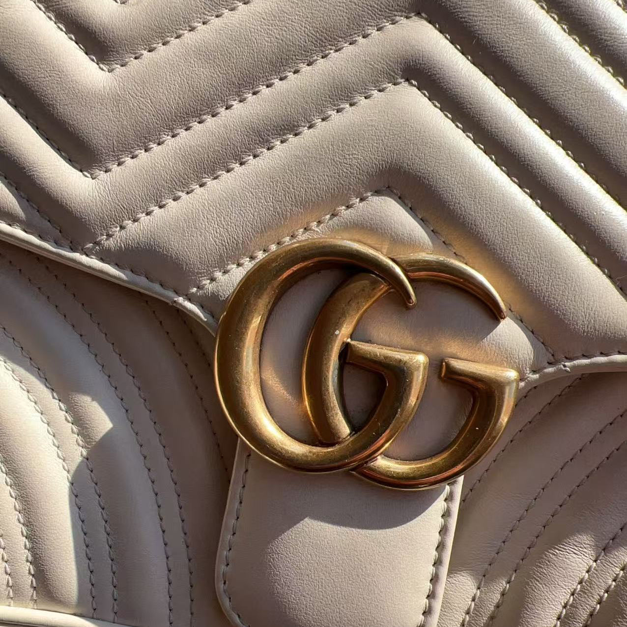 Close-up of a beige quilted handbag with a gold Gucci logo.