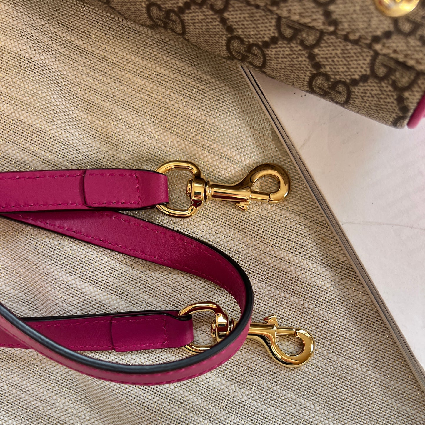 Close-up of a purple handbag strap with gold hardware on a textured beige background