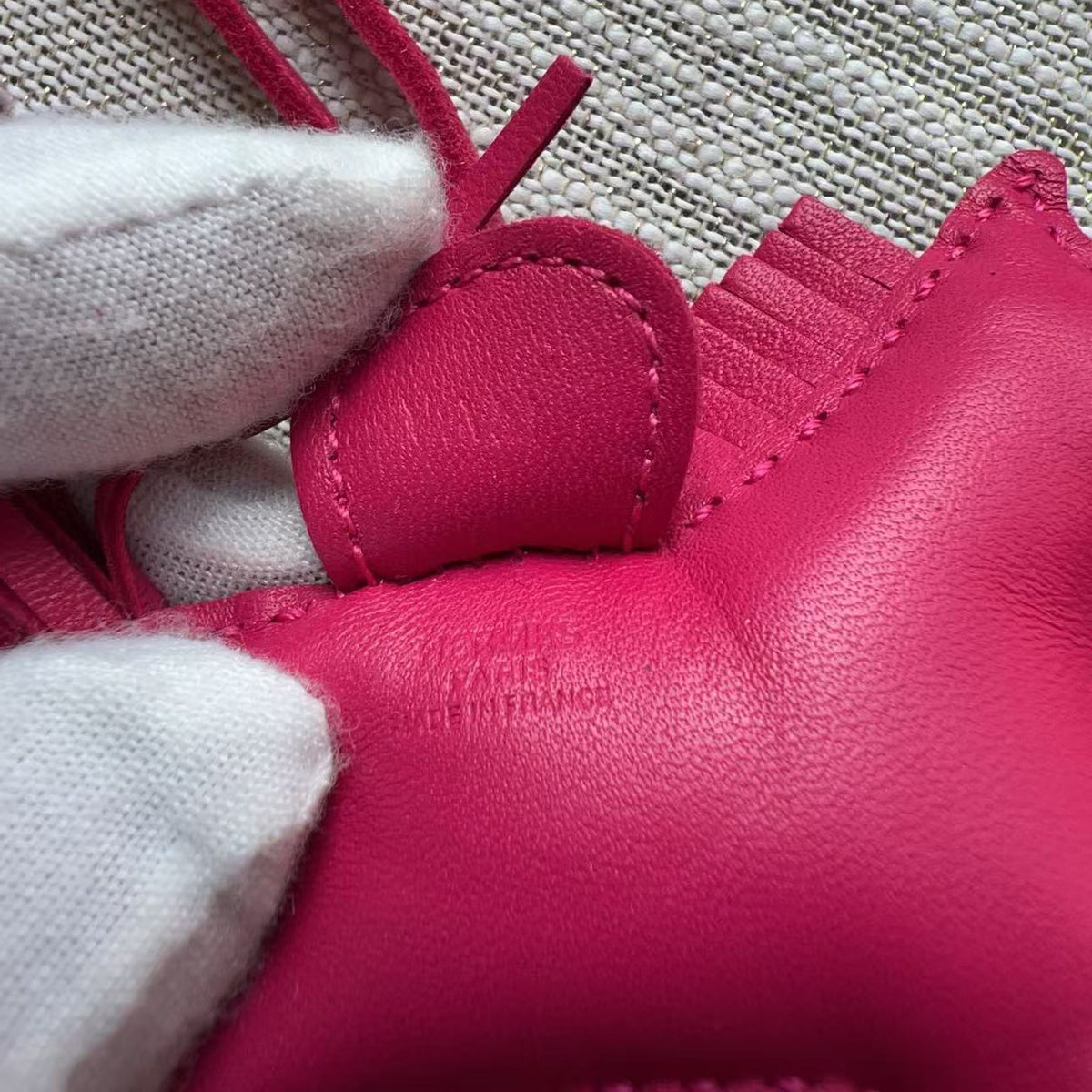 Close-up of a bright pink leather shoe or boot interior with visible stitching, a small heart-shaped leather tab, and white knit or felt lining around the opening.