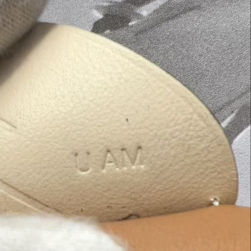 Close-up of a beige leather shoe insole with the debossed letters 'UAM' on a gray and white patterned fabric background.