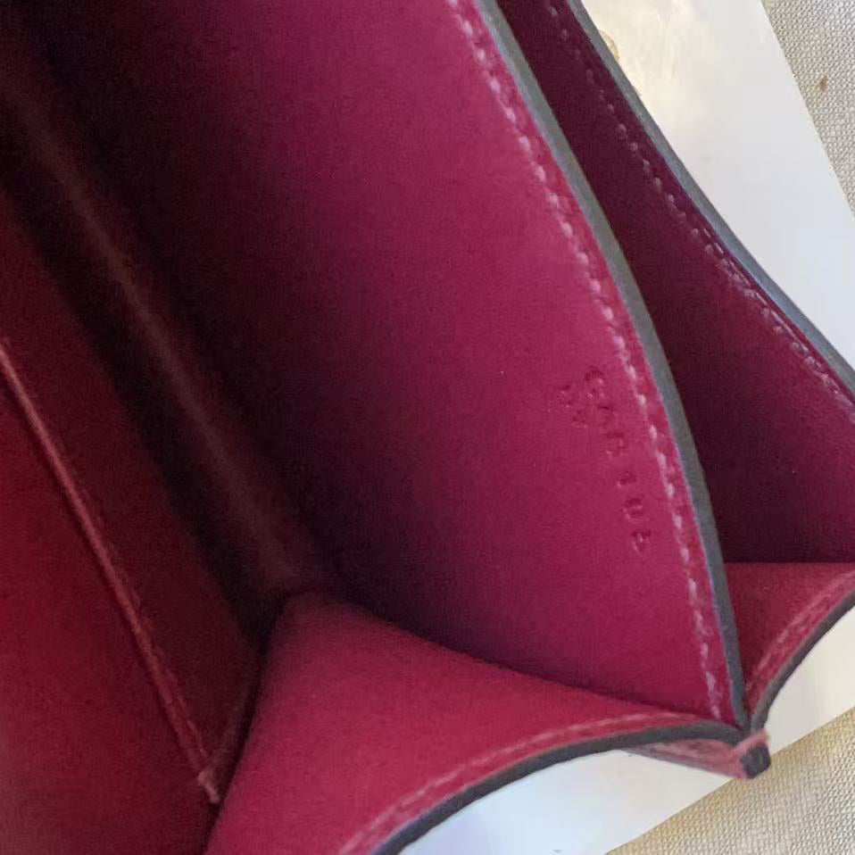 Close-up of the interior of a burgundy leather wallet or card case, showing stitched compartments and a finger holding the edge to demonstrate depth, on a light beige textured surface.