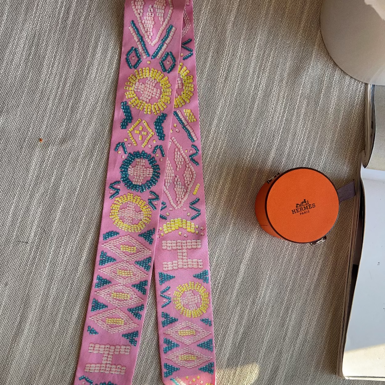 Pink embroidered headband with colorful patterns on a textured surface next to an orange container.