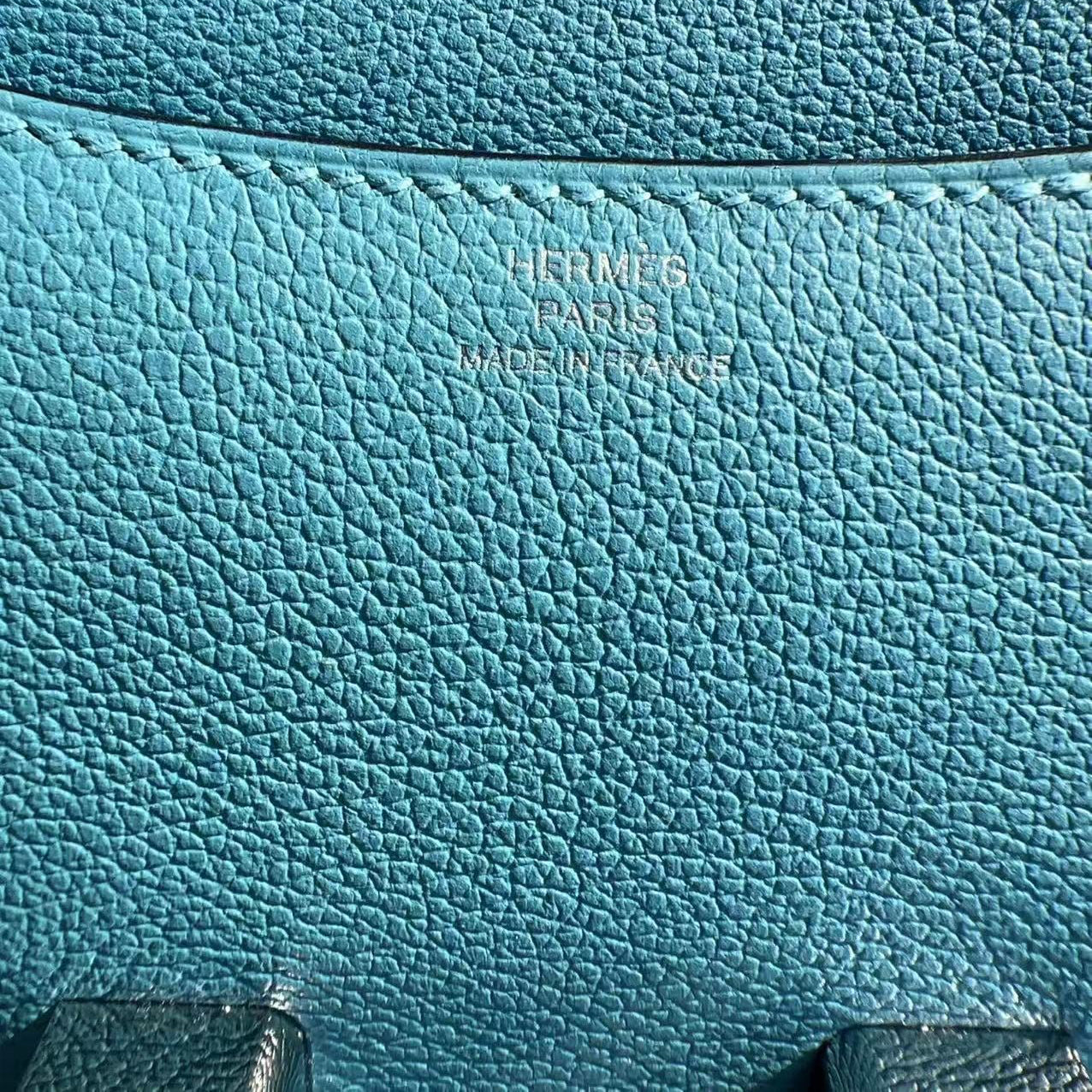 Close-up of a blue leather bag with 'Hermes' branding.