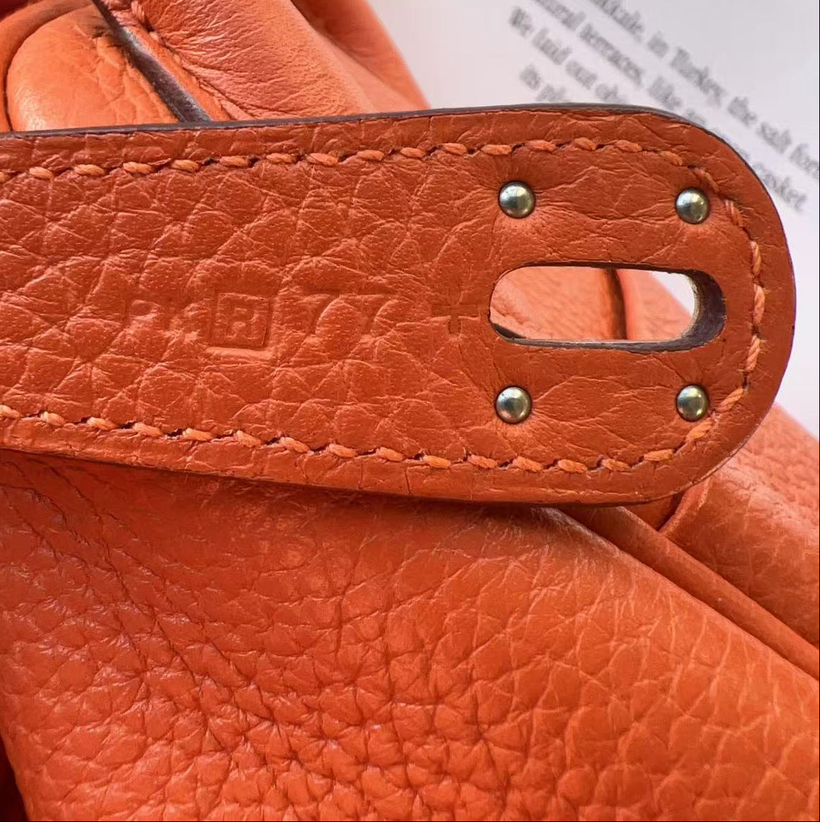 Close-up of an orange leather handbag with visible stitching and hardware.