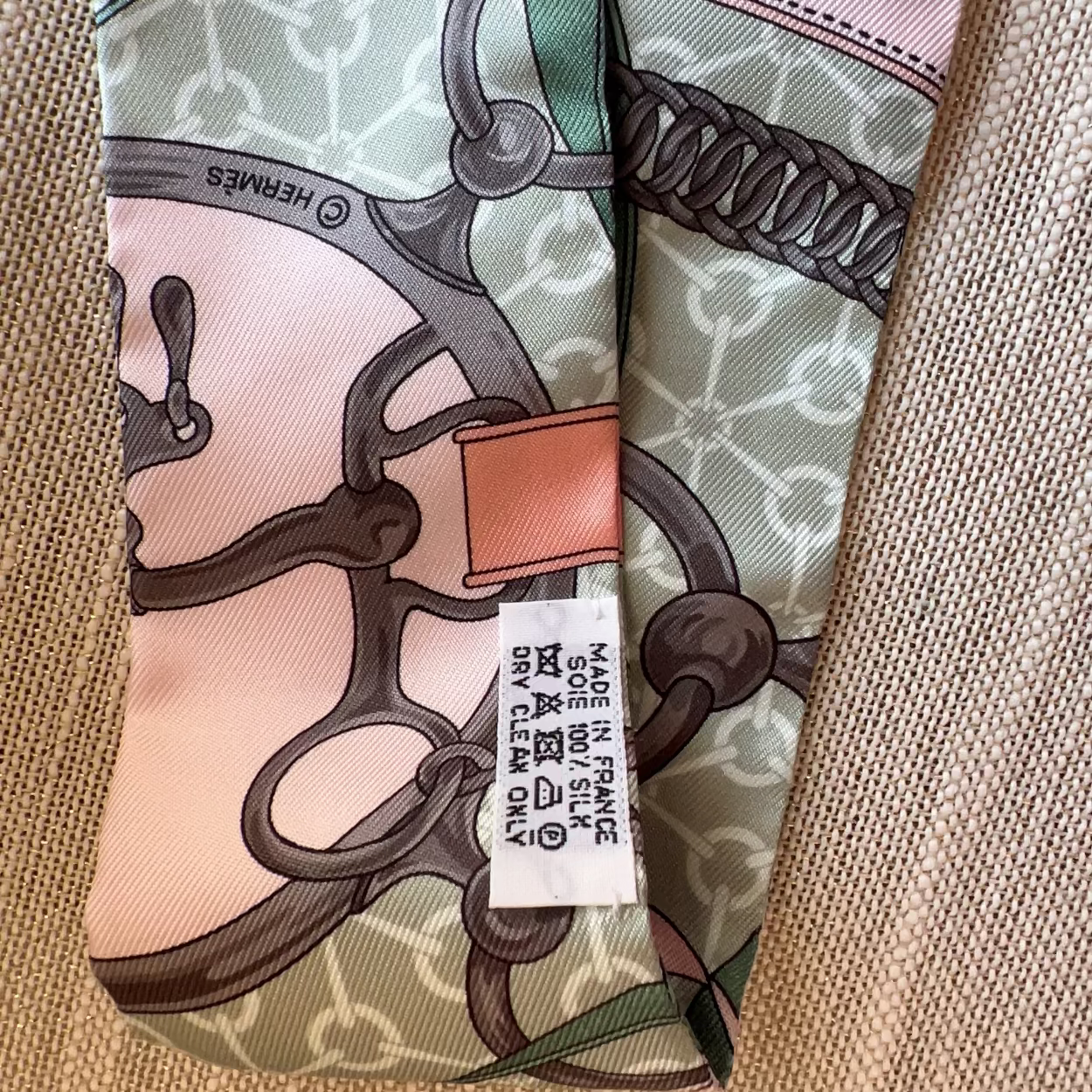 Hermes scarf with intricate design and brand label on a textured surface