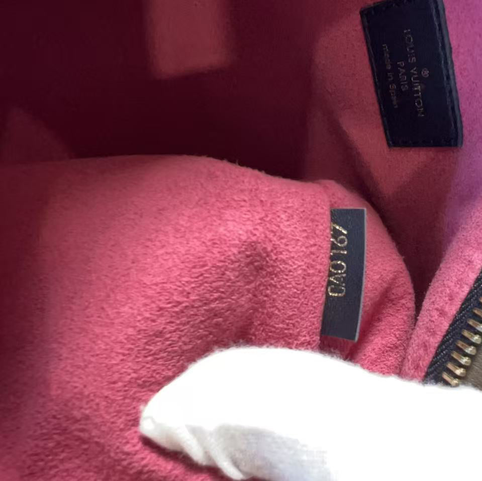 Close-up of a Louis Vuitton handbag interior showing a pink suede lining, a black leather brand label, a gold-tone zipper, and a white gloved hand touching the lining.