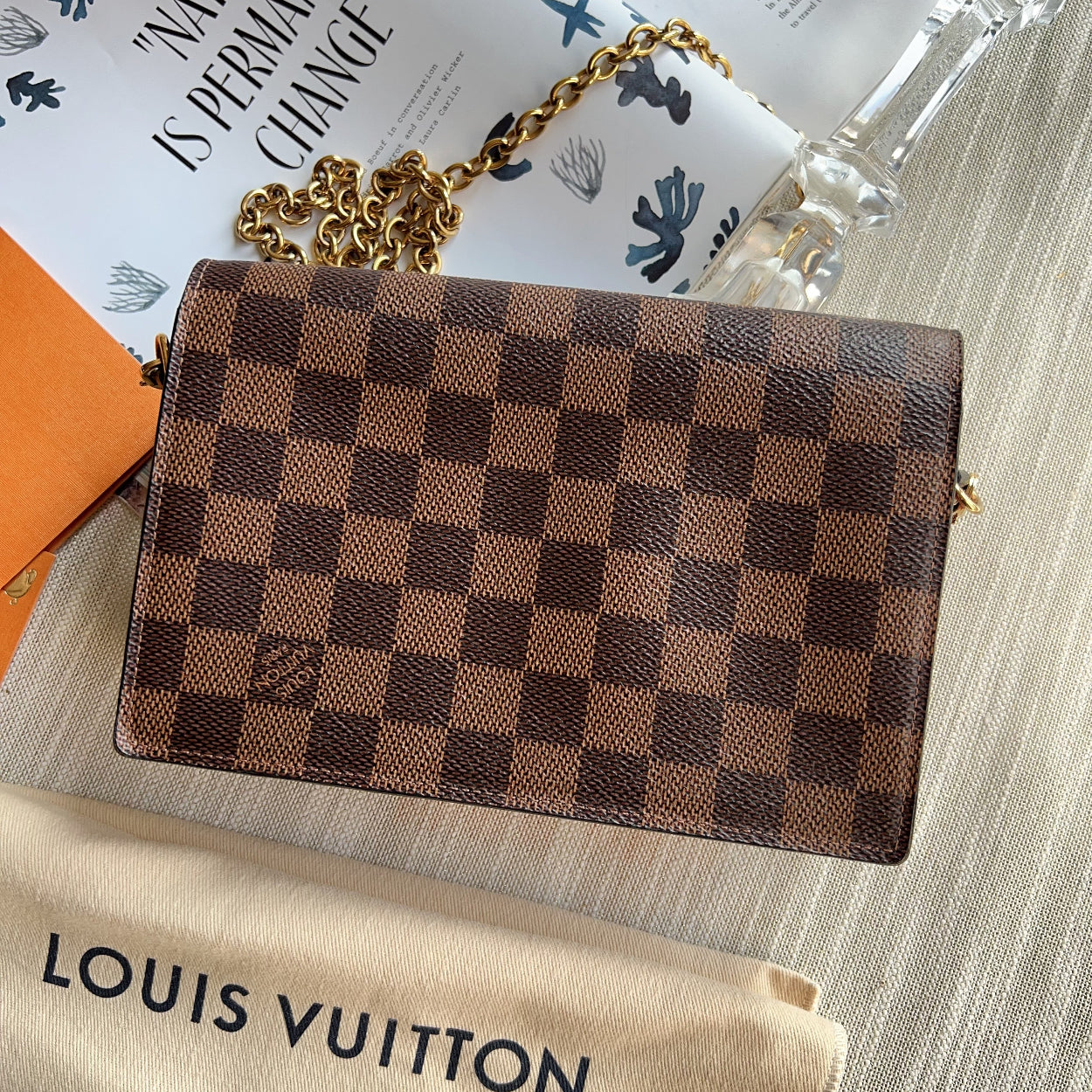 Louis Vuitton wallet with checkered pattern on a surface with a branded pouch underneath.