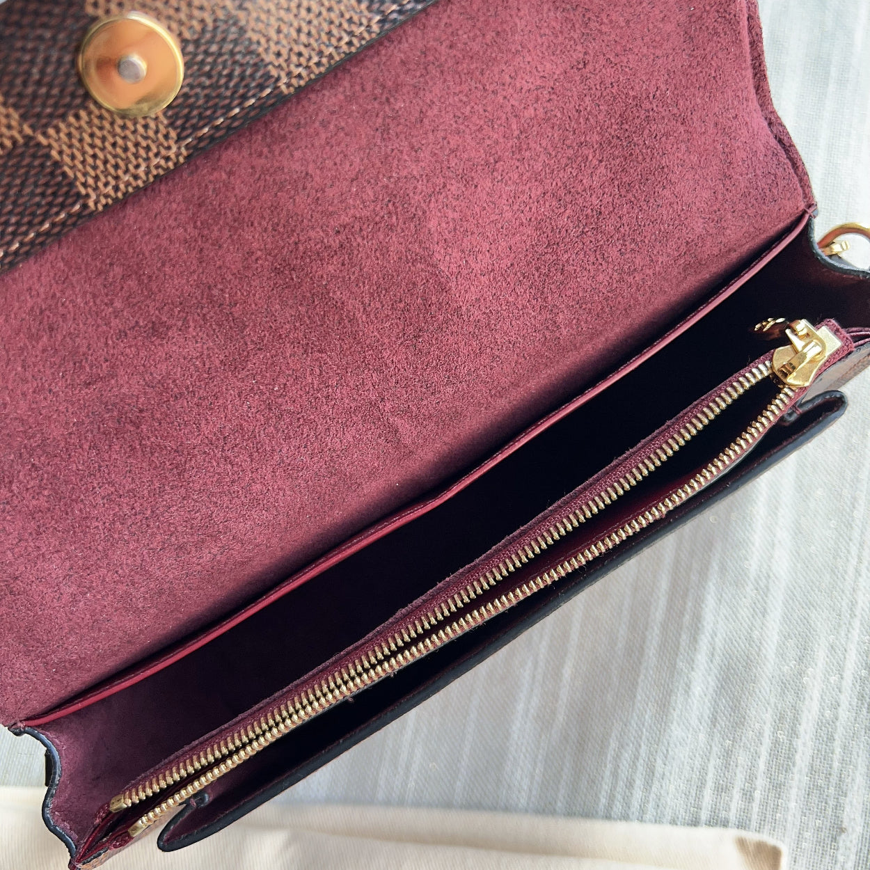Close-up of a maroon clutch bag with gold zipper and patterned fabric on top.
