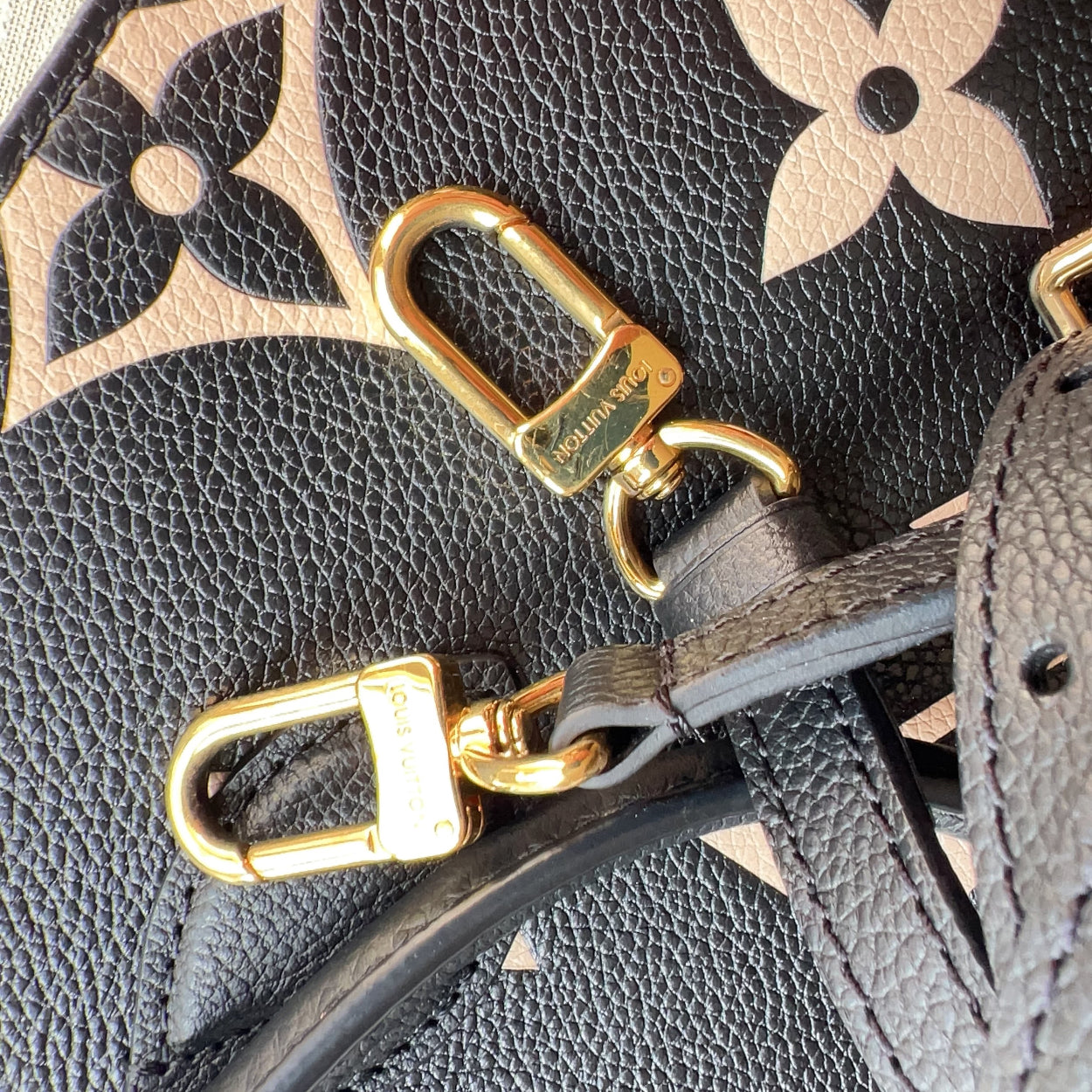 Close-up of a Louis Vuitton handbag with gold hardware on a textured surface.