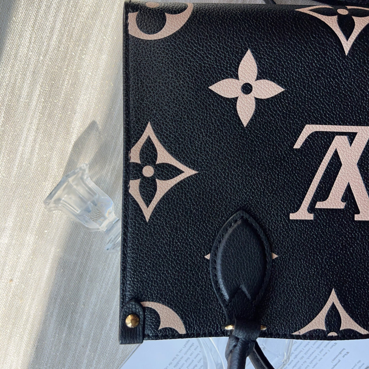 Black pouch with beige monogram pattern on a light gray surface