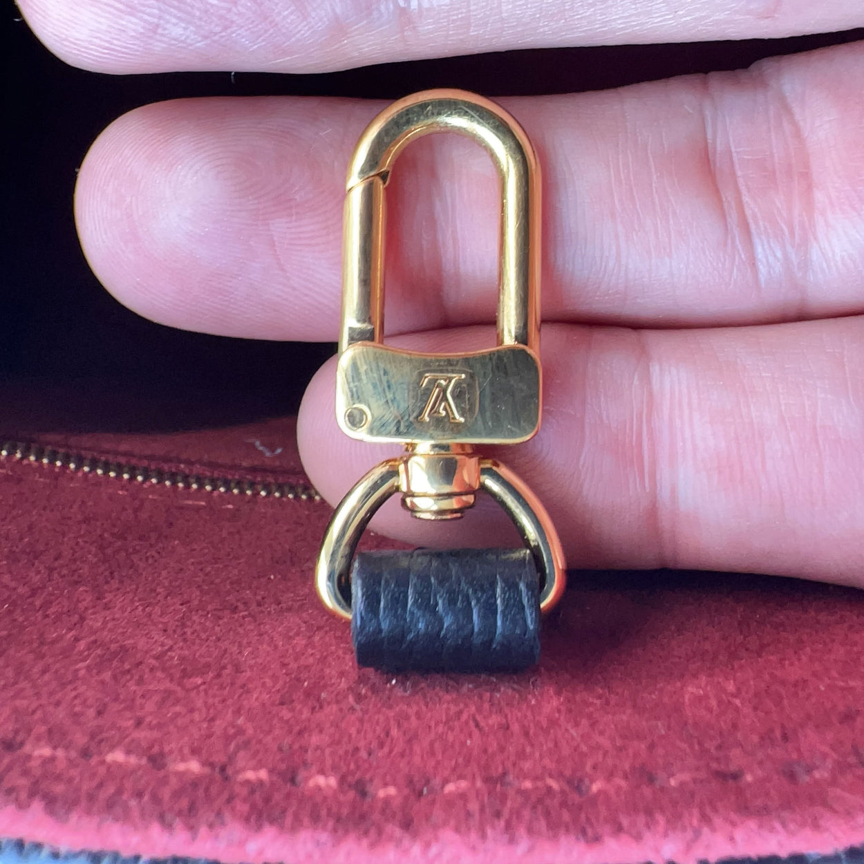 Gold carabiner with a black strap end held between fingers against a red fabric background