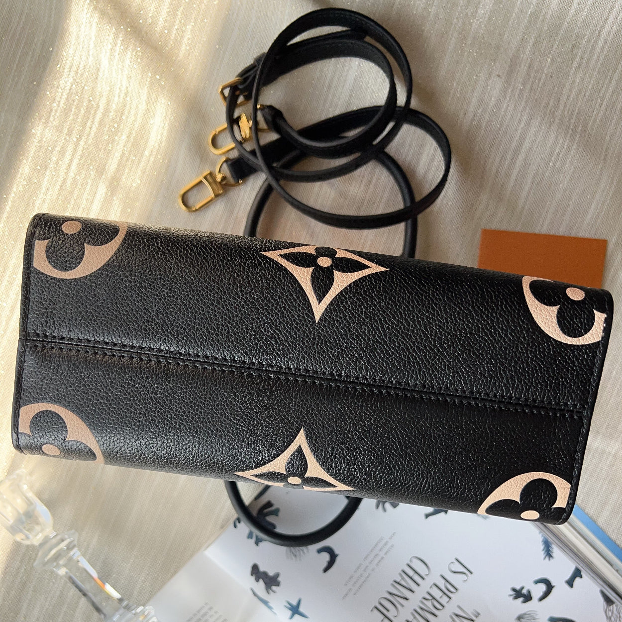 Black wallet with beige patterns on a surface with a book and glass.