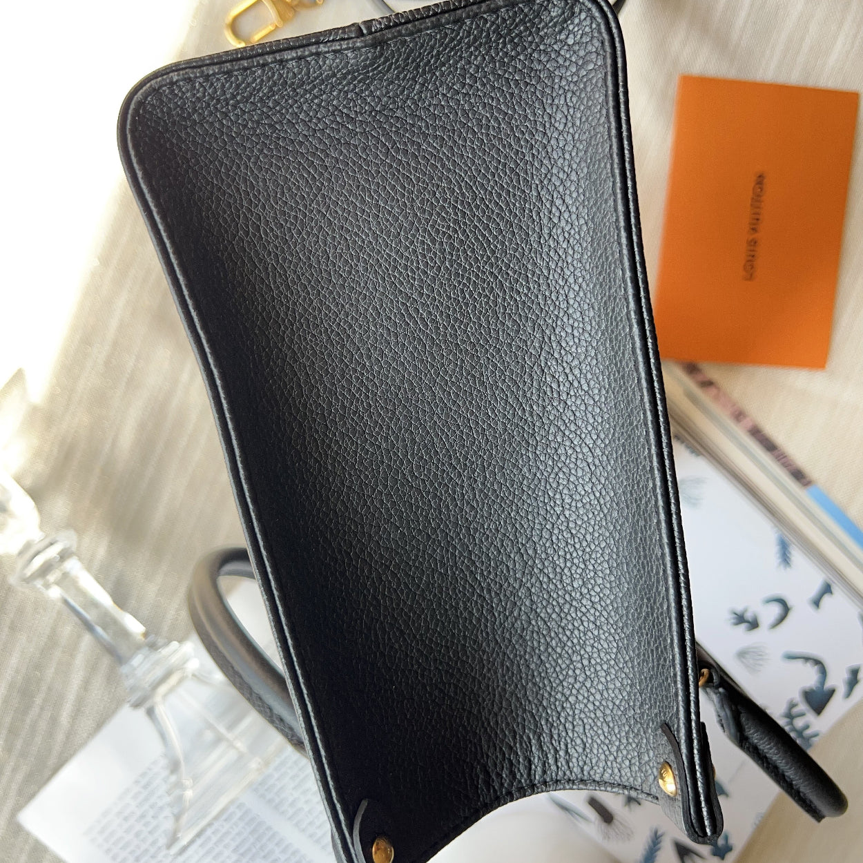 Black leather pouch on a textured surface with a visible brand name.