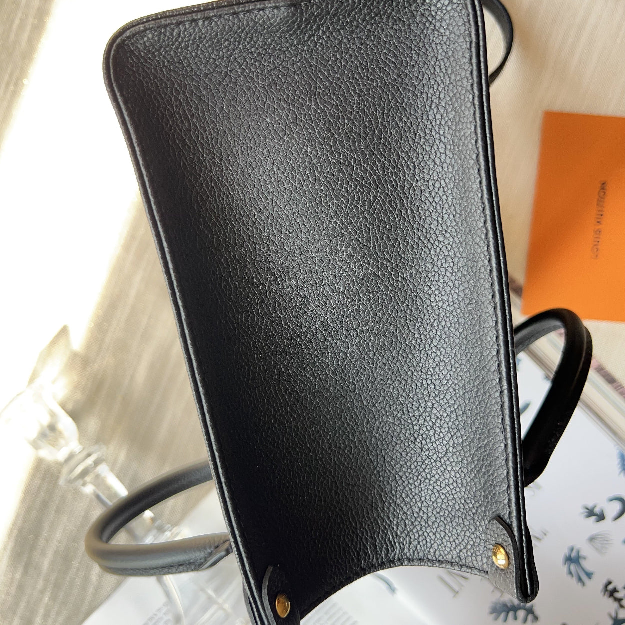 Black leather clutch bag on a white surface with a blurred background