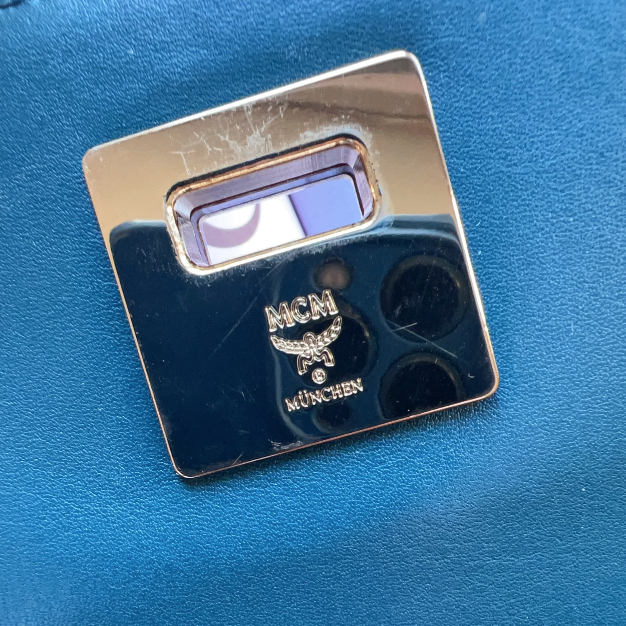 Metallic square object with 'MCM München' logo on a blue background