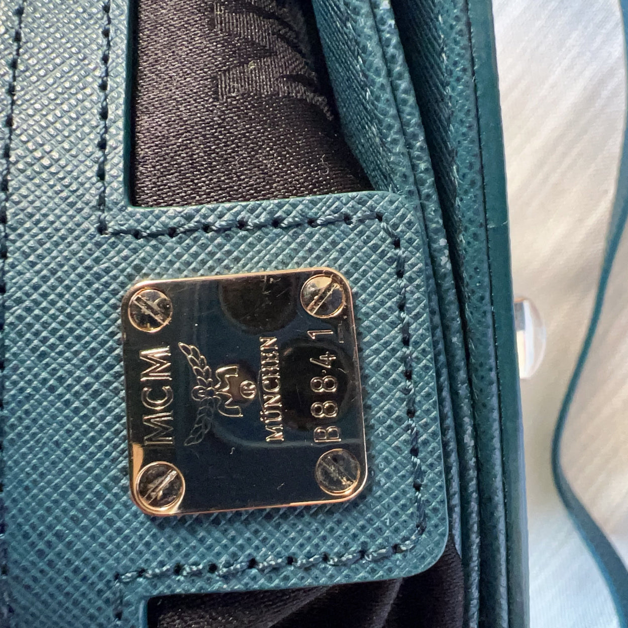 Close-up of a teal handbag with a gold and black label.