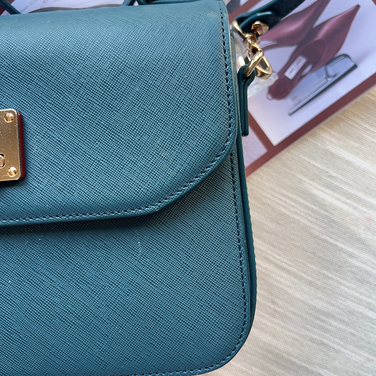 Teal handbag with gold clasp on a light wooden surface