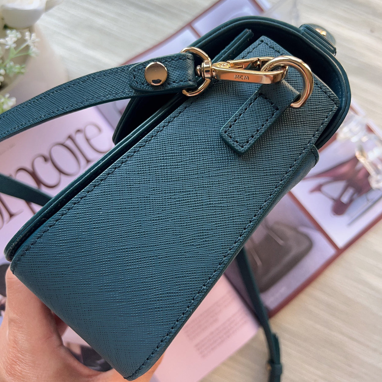 Green handbag with gold hardware held by a hand on a blurred background