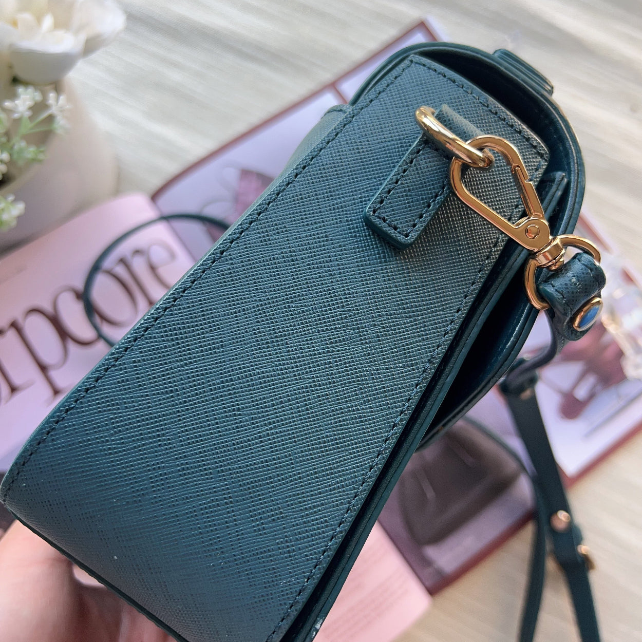 Teal handbag with gold clasp held by a hand on a blurred background