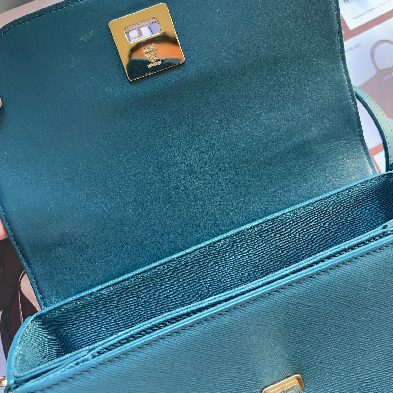Teal handbag with a gold logo on a blurred background
