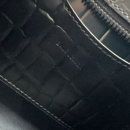 Close-up of a black crocodile-embossed leather zipper pull and trim with white stitching.