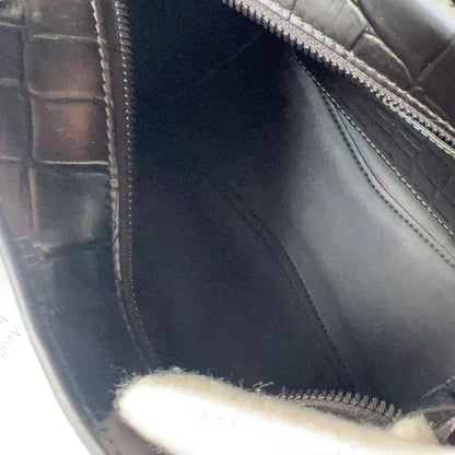 Close-up of the interior of a black crocodile-embossed leather bag, showing the black fabric lining and zipper, with a white gloved hand holding the opening.
