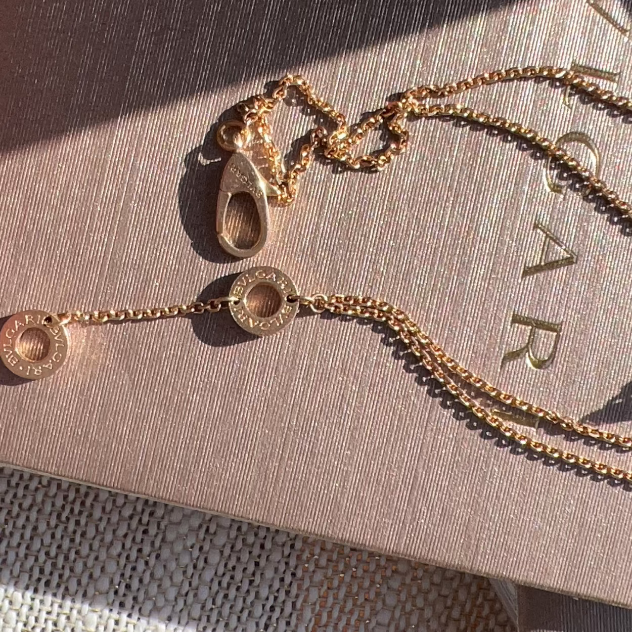 Gold necklace on a textured surface with 'Bvlgari' branding.