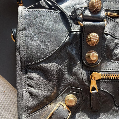 Close-up of a gray leather bag with gold accents on a wooden surface.