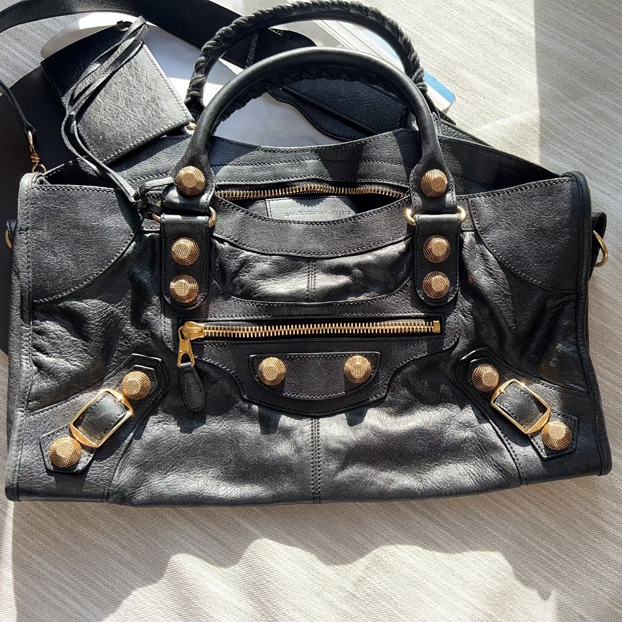 Black leather bag with gold studs and zippers on a light wooden surface.