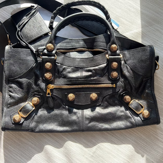 Black leather bag with gold studs and zippers on a light wooden surface.