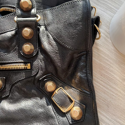 Close-up of a black leather bag with gold hardware on a light wooden surface.