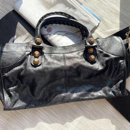 Black leather handbag with gold accents on a light wooden surface
