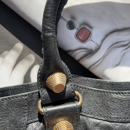 Close-up of a black leather handbag with gold hardware on a marble surface.